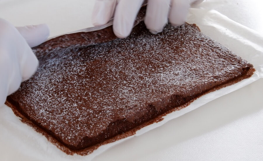 Freshly-baked chocolate sponge looking soft and being rolled without cracking.